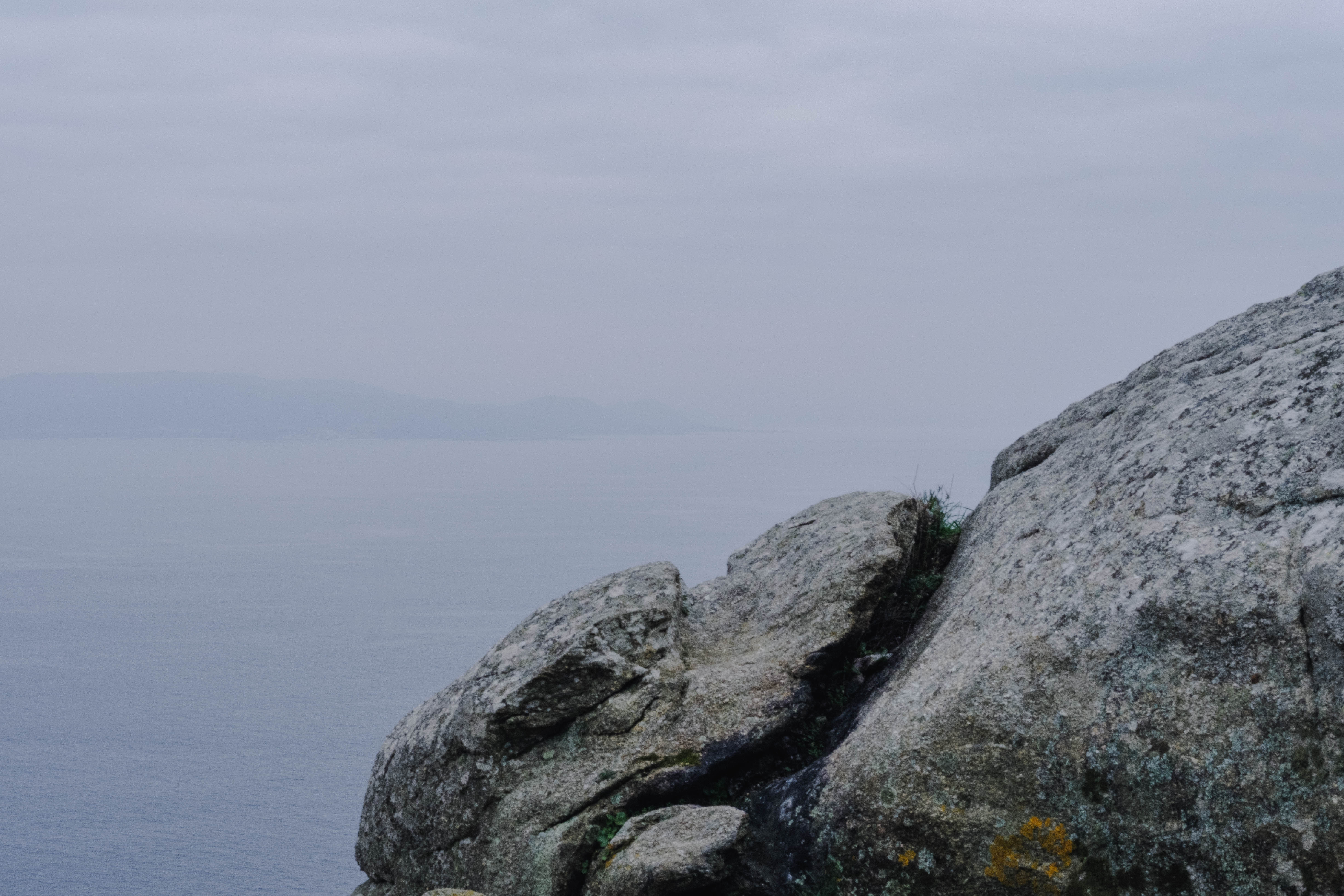 Weathered granite rock formation on a headland overlooking a calm, misty sea, with distant hills faintly visible on the horizon.