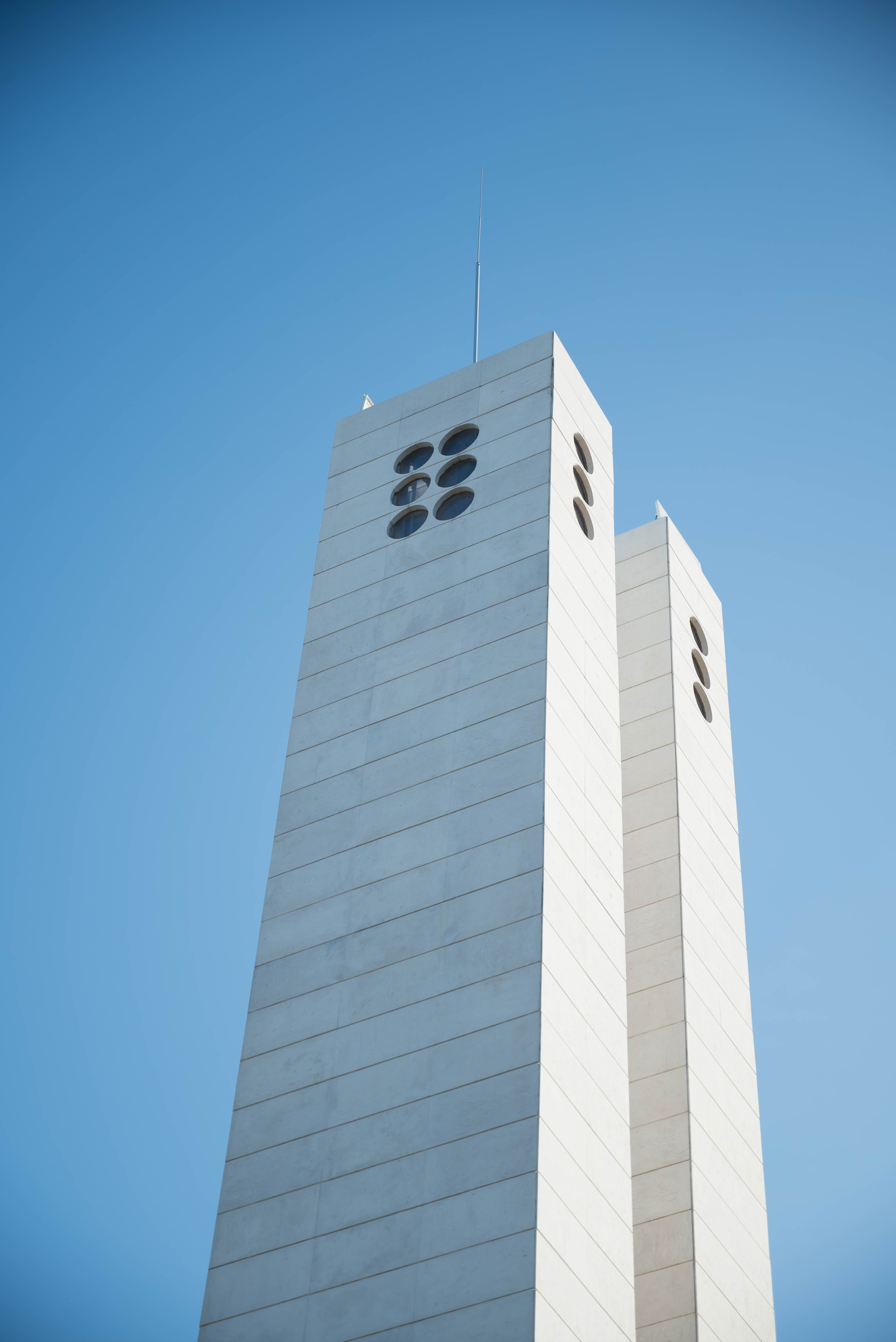 Low-angle view of two tall white concrete towers with oval-shaped windows, set against a clear deep blue sky.
