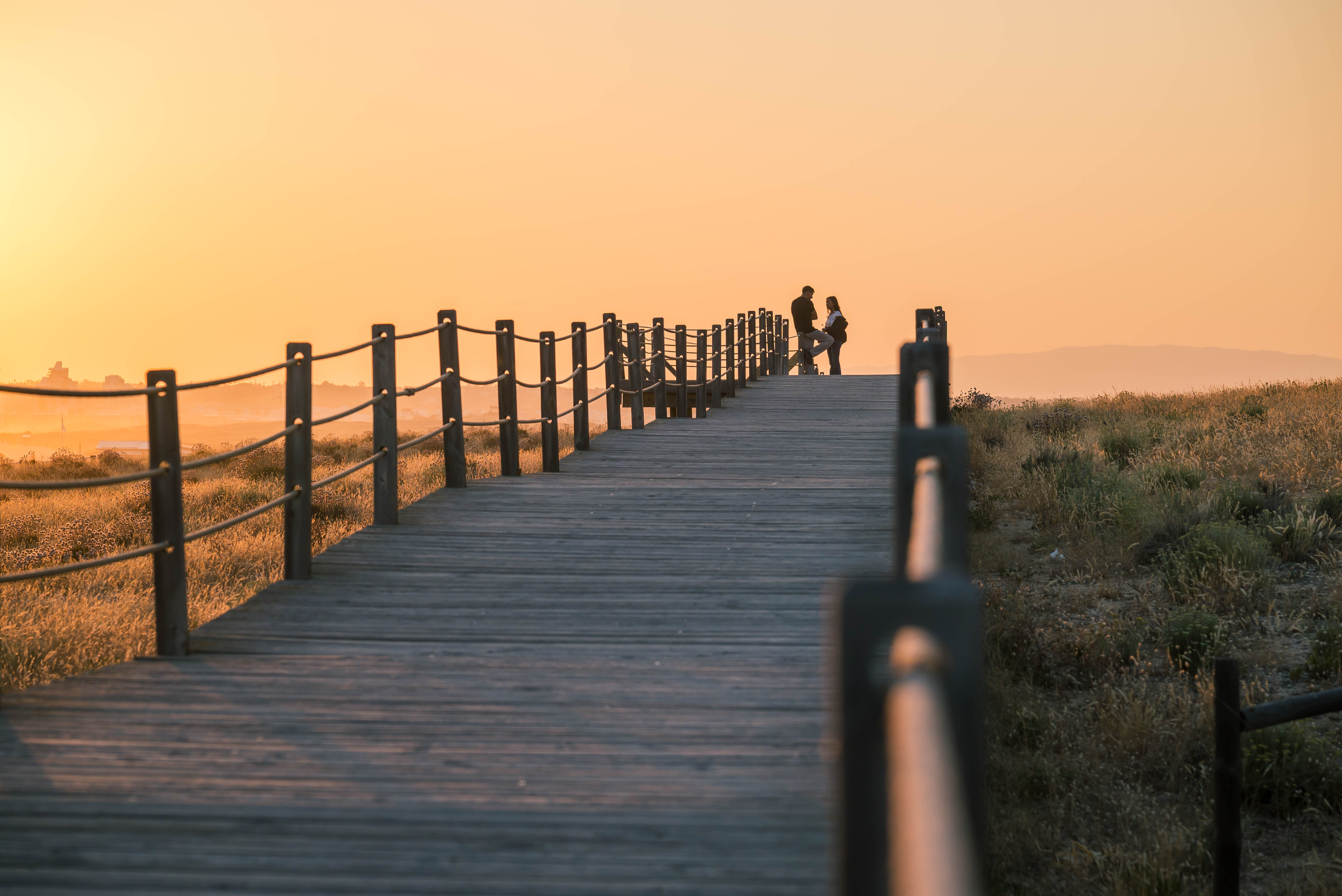 A couple on the horizon in a promenade by the beach during sunset