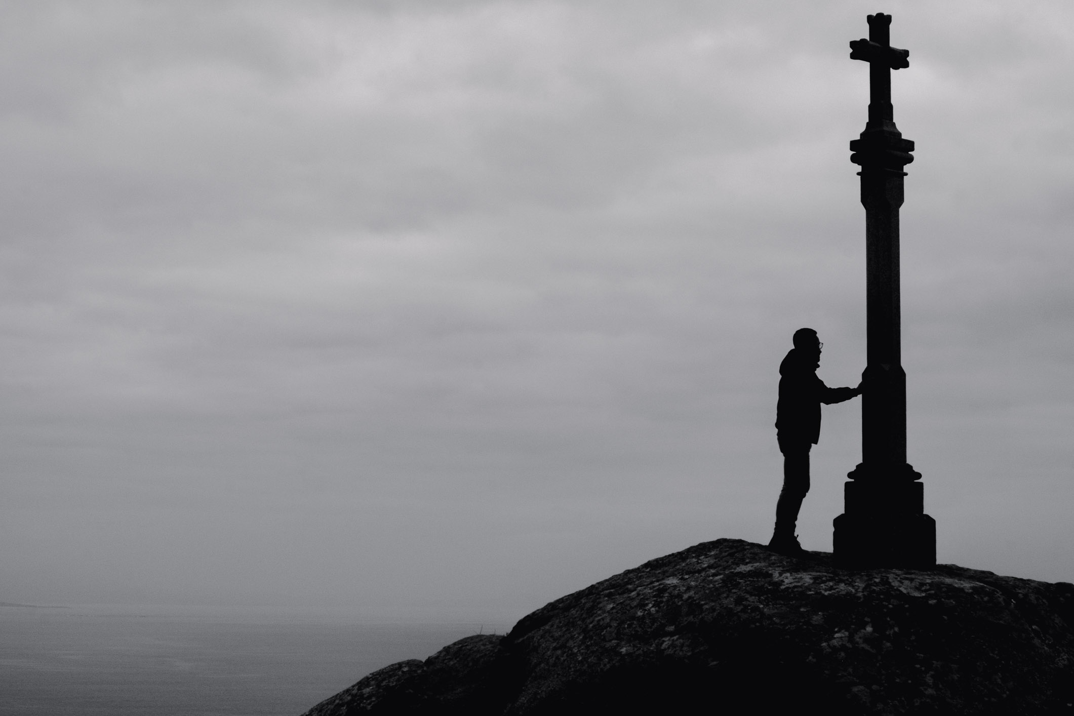 Man on top of rock with his hand on a stone cross